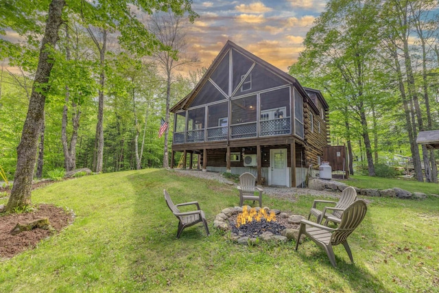 3233 Stinson Lake Rd, Ellsworth, NH 03266 - back of property at dusk featuring an outdoor fire pit, a sunroom, a lawn, and a wooden deck