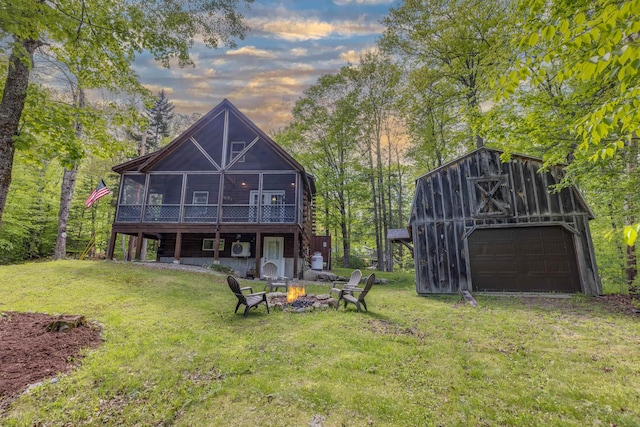 3233 Stinson Lake Rd, Ellsworth, NH 03266 - rear view of house featuring a detached garage, a fire pit, an outdoor structure, a lawn, and a sunroom