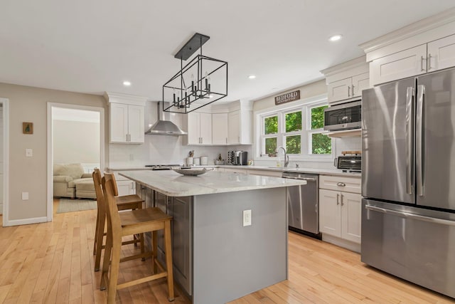78 Hitching Post Ln, Bedford, NH 03110 - kitchen with stainless steel appliances, wall chimney exhaust hood, a sink, light wood-style flooring, and tasteful backsplash
