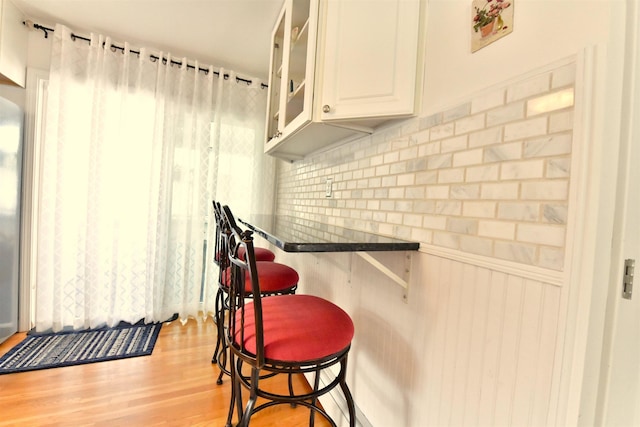55 Harding St, Manchester, NH 03109 - kitchen featuring a breakfast bar, light wood-style flooring, decorative backsplash, glass insert cabinets, and white cabinetry