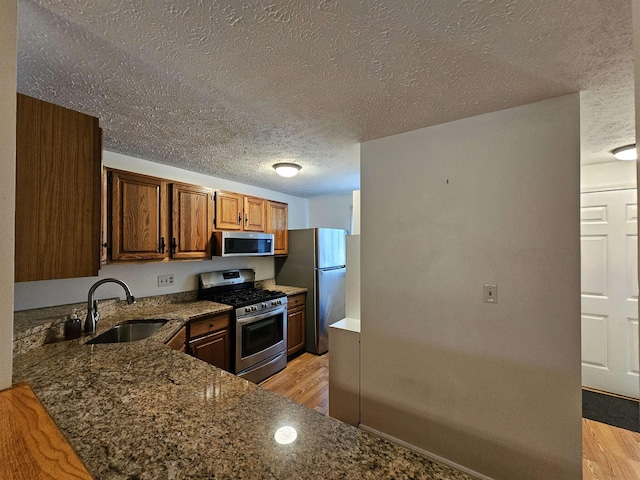 302 Eastview Dr, Wilton, NH 03086 - kitchen with stainless steel appliances, a sink, a textured ceiling, light wood-type flooring, and dark stone counters