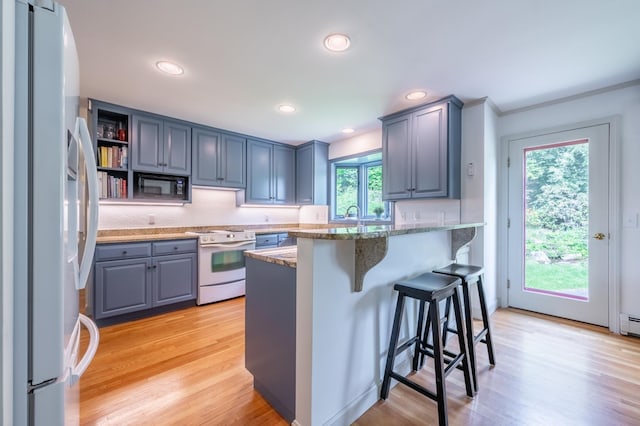 51 Carter Rd, New London, NH 03257 - kitchen featuring white appliances, a kitchen bar, light wood-type flooring, light stone counters, and a peninsula