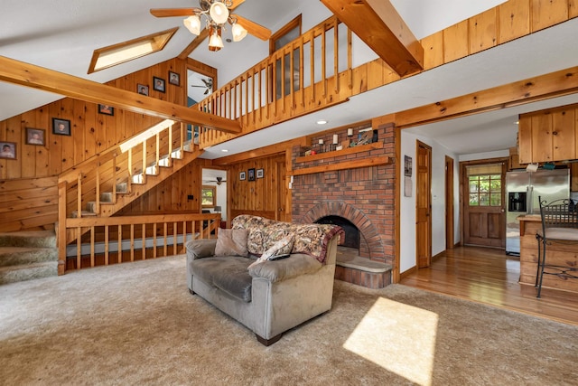 222 Main St, Alton, NH 03809 - carpeted living area with a ceiling fan, wood walls, stairway, a skylight, and a brick fireplace