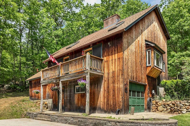 222 Main St, Alton, NH 03809 - view of front facade featuring a garage, a shingled roof, a chimney, and a balcony