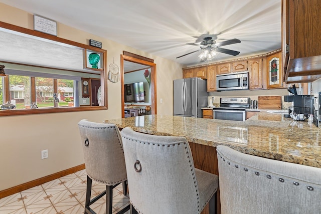 396 Huse Rd, Manchester, NH 03103 - kitchen with stainless steel appliances, a peninsula, baseboards, brown cabinets, and light stone counters