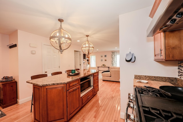 65 Victoria St Unit 8, Manchester, NH 03104 - kitchen with extractor fan, a chandelier, stainless steel gas stove, brown cabinets, and light wood-style flooring