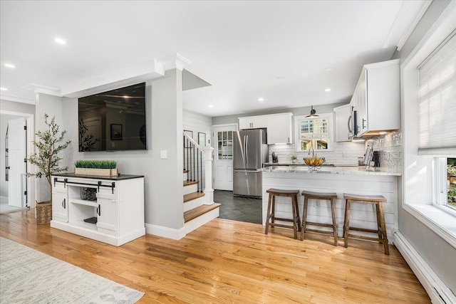 85 Lee Ave, Manchester, NH 03109 - kitchen featuring appliances with stainless steel finishes, a baseboard heating unit, a peninsula, white cabinets, and light wood-style floors
