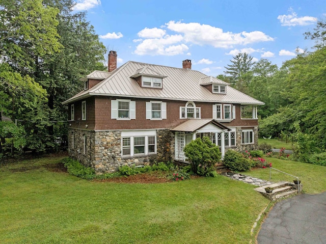 shingle-style home featuring stone siding, a standing seam roof, a chimney, a front lawn, and metal roof