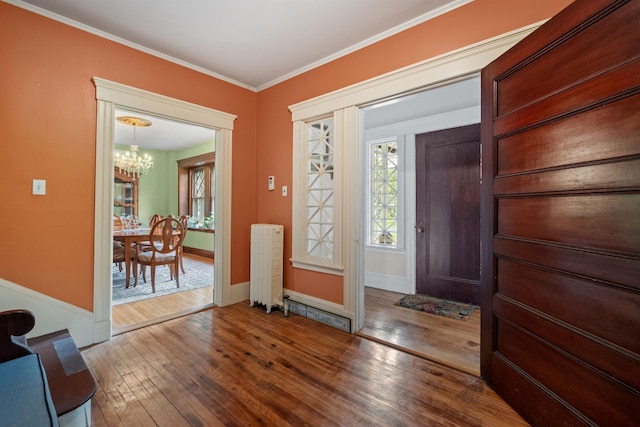 foyer entrance with hardwood / wood-style flooring, a chandelier, crown molding, radiator heating unit, and baseboards