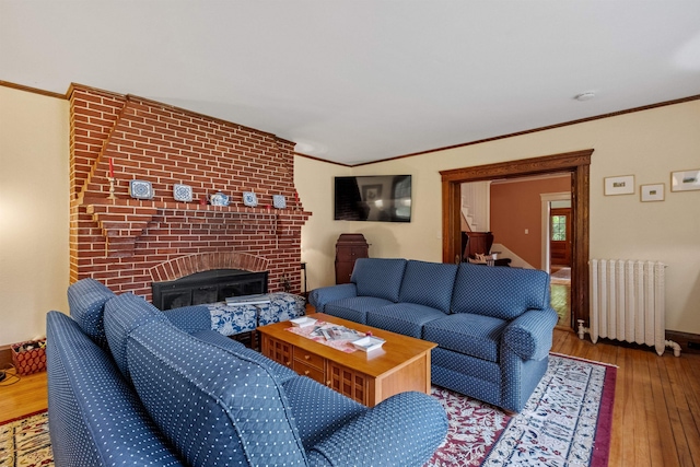 living area with radiator, wood-type flooring, a brick fireplace, ornamental molding, and baseboards