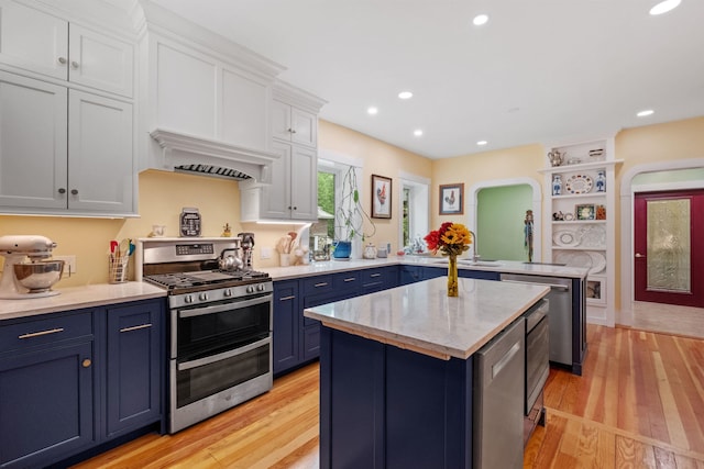 kitchen featuring stainless steel appliances, blue cabinets, a peninsula, light wood-style floors, and white cabinets