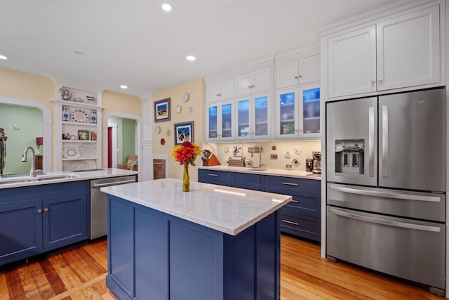 kitchen with stainless steel appliances, blue cabinets, a sink, arched walkways, and recessed lighting