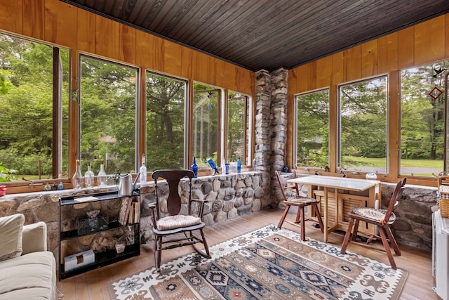 sunroom featuring a wooden deck, wood walls, healthy amount of natural light, hardwood / wood-style flooring, and vaulted ceiling