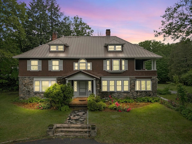 view of front of house featuring a chimney, a standing seam roof, stone siding, and a front lawn