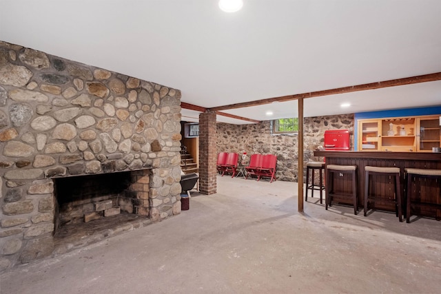 living area with a dry bar, a stone fireplace, and unfinished concrete floors