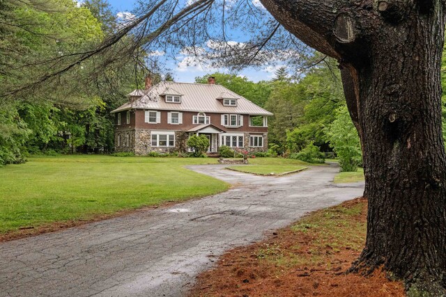 view of front of home featuring a chimney, stone siding, driveway, a front yard, and metal roof