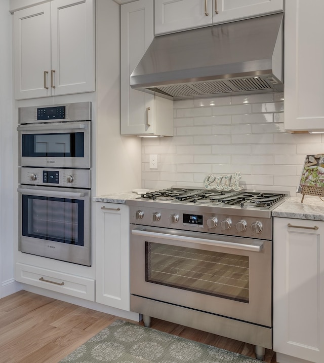 338 Pine Hill Rd, Hollis, NH 03049 - kitchen with appliances with stainless steel finishes, ventilation hood, light wood-style floors, light stone counters, and backsplash