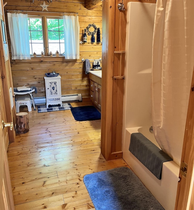 27 Stearns Ave, Wilmington, VT 05363 - bathroom with wooden walls, wood-type flooring, baseboard heating, vanity, and shower / tub combo with curtain