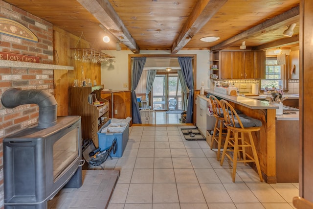 10 Mountain View Ter, Plymouth, NH 03264 - kitchen with wooden ceiling with exposed beams, a wood stove, brown cabinetry, open shelves, and light tile patterned floors