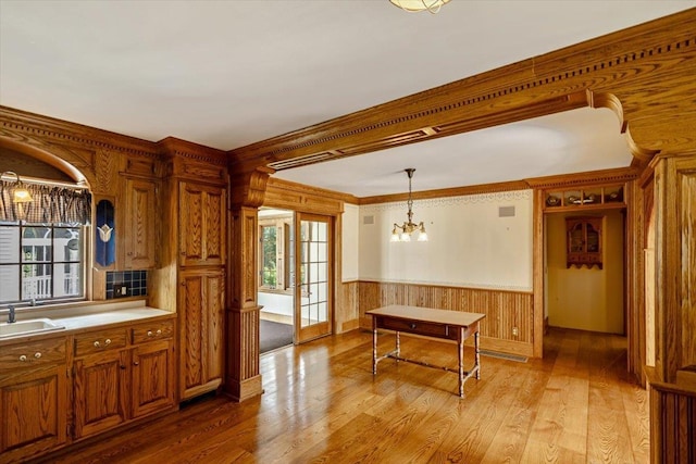 98 Sugar Maple Dr, Swanton, VT 05488 - kitchen with a chandelier, light wood finished floors, brown cabinetry, a sink, and a wainscoted wall