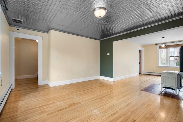 647 Canal St, Manchester, NH 03101 - unfurnished room with a baseboard radiator, light wood-style flooring, baseboards, a wood stove, and crown molding