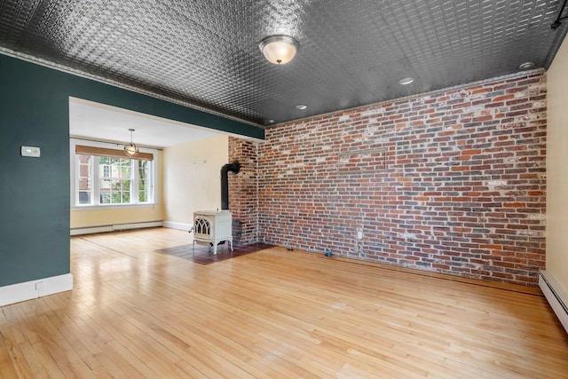 647 Canal St, Manchester, NH 03101 - unfurnished living room featuring brick wall, a wood stove, a baseboard heating unit, baseboards, and wood-type flooring