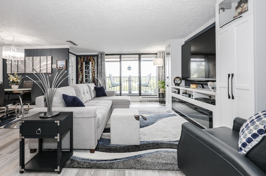 55 River Rd Unit 8D, Manchester, NH 03104 - living room with wood finished floors, a chandelier, a textured ceiling, and floor to ceiling windows