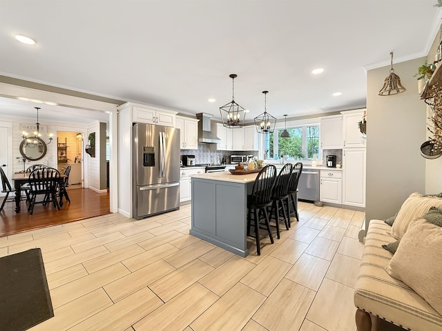 128 Gale St, Canaan, VT 05903 - kitchen with appliances with stainless steel finishes, a chandelier, wall chimney range hood, white cabinetry, and ornamental molding