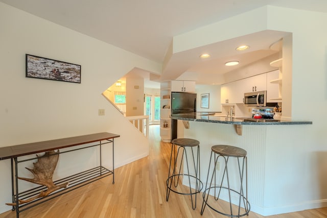 58 Bunker Ln Unit 3, Lincoln, NH 03251 - kitchen with appliances with stainless steel finishes, open shelves, white cabinets, a kitchen bar, and light wood-type flooring