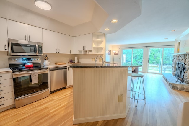 58 Bunker Ln Unit 3, Lincoln, NH 03251 - kitchen with stainless steel appliances, light wood-style flooring, open shelves, a breakfast bar, and white cabinetry