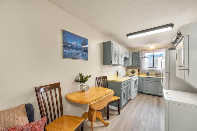 42 Wylie Ct Unit 6, Conway, NH 03860 - kitchen with white range with electric cooktop, gray cabinets, light wood-style floors, stacked washer and clothes dryer, and a textured ceiling