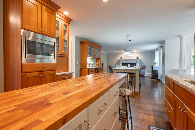 35 Fletcher Ln, Hollis, NH 03049 - kitchen with wooden counters, stainless steel microwave, decorative columns, brown cabinetry, and open floor plan