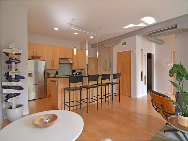 161 St Paul St Unit 202, Burlington, VT 05401 - kitchen featuring stainless steel fridge with ice dispenser, under cabinet range hood, light wood finished floors, a breakfast bar, and dark countertops