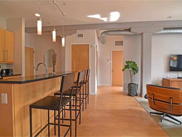 161 St Paul St Unit 202, Burlington, VT 05401 - kitchen with a breakfast bar, dark countertops, light wood-type flooring, pendant lighting, and a kitchen island with sink