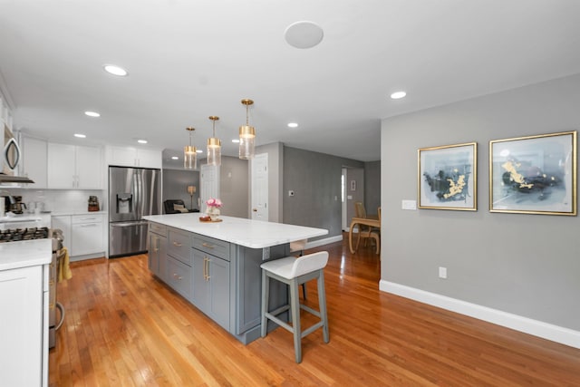 12 Julia Dr, Hooksett, NH 03106 - kitchen with stainless steel appliances, white cabinets, light wood-style flooring, light countertops, and a breakfast bar