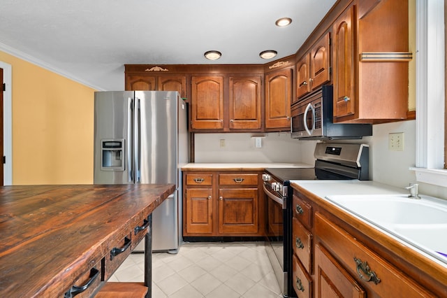 90 Giles Rd, East Kingston, NH 03827 - kitchen featuring appliances with stainless steel finishes, light tile patterned floors, brown cabinets, crown molding, and recessed lighting