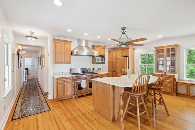 68 Sewall Rd, Wolfeboro, NH 03894 - kitchen featuring wall chimney exhaust hood, high end appliances, light wood-style flooring, a ceiling fan, and a center island with sink