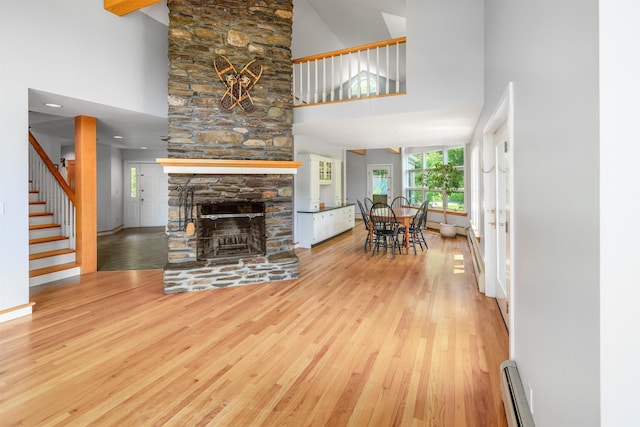 650 Perry Lea Rd, Waterbury, VT 05676 - living area featuring high vaulted ceiling, wood finished floors, a baseboard heating unit, a stone fireplace, and stairs