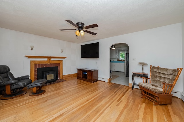 10 Eastern Ave, Rochester, NH 03867 - living area with a ceiling fan, a baseboard heating unit, arched walkways, light wood finished floors, and a fireplace
