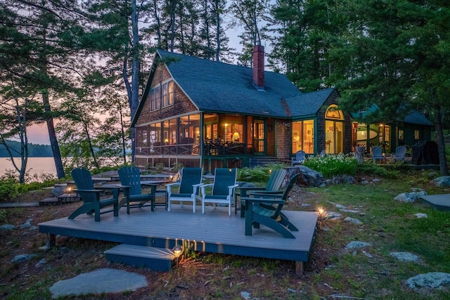 310 Bear Is, Meredith, NH 03253 - back of house at dusk with a sunroom, a wooden deck, a chimney, and a shingled roof