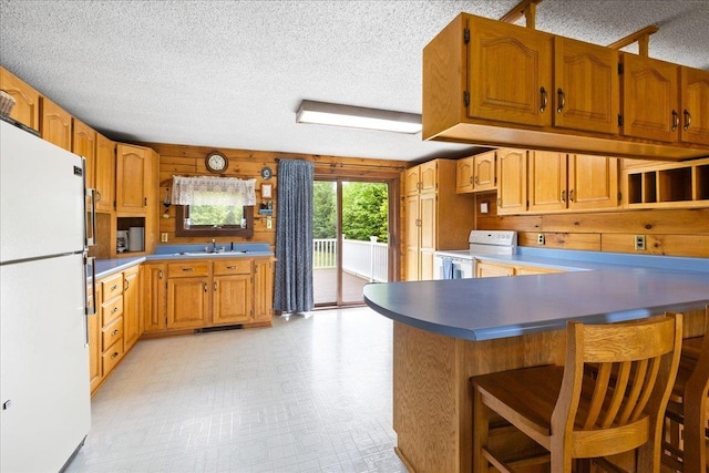 110 W Milan Rd, Milan, NH 03588 - kitchen featuring white appliances, a peninsula, a textured ceiling, a breakfast bar, and brown cabinetry