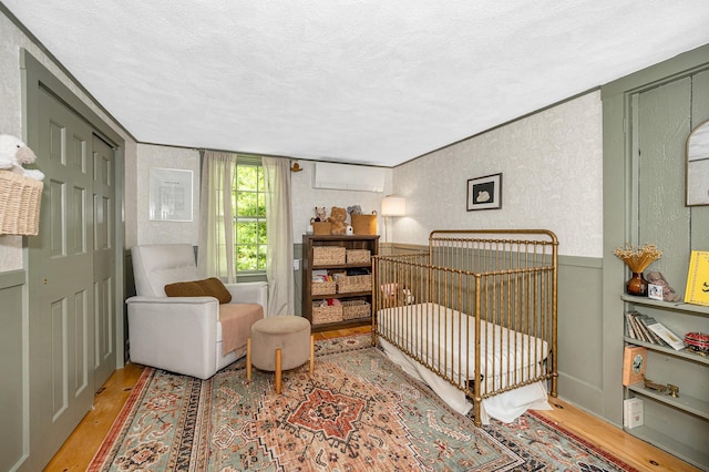 8 Main St, Brookline, NH 03033 - bedroom featuring wood finished floors, a textured ceiling, a crib, and a wall mounted air conditioner