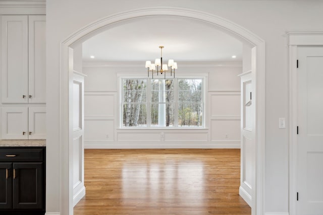 131 Exeter Rd, North Hampton, NH 03862 - unfurnished dining area with arched walkways, light wood-type flooring, a chandelier, a decorative wall, and ornamental molding