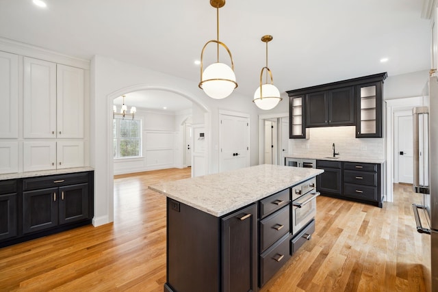131 Exeter Rd, North Hampton, NH 03862 - kitchen featuring arched walkways, appliances with stainless steel finishes, light wood-style flooring, decorative backsplash, and glass insert cabinets