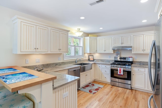 5 Fellows Ave, Hampton, NH 03842 - kitchen with appliances with stainless steel finishes, under cabinet range hood, a peninsula, light wood-type flooring, and light stone counters