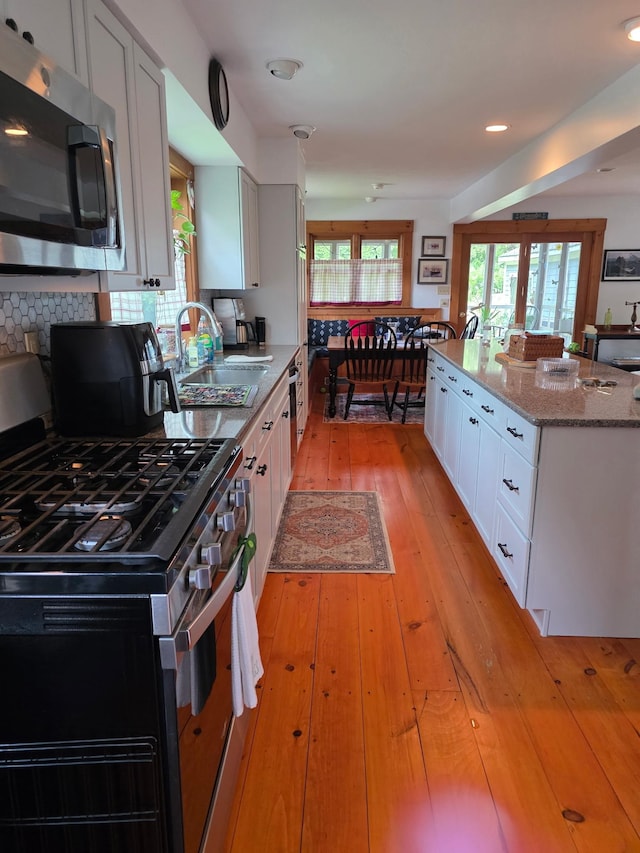 104 Middle St, Lancaster, NH 03584 - kitchen with stainless steel appliances, white cabinets, light stone counters, light wood-style flooring, and tasteful backsplash