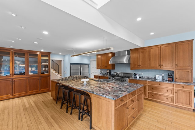 214 Upper Hollow Rd, Stowe, VT 05672 - kitchen featuring wall chimney range hood, stainless steel fridge, light wood finished floors, range, and a breakfast bar area