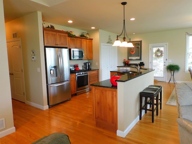 150 Pleasant Pond Way Unit 15, Manchester, NH 03102 - kitchen with appliances with stainless steel finishes, brown cabinetry, light wood finished floors, a breakfast bar, and recessed lighting