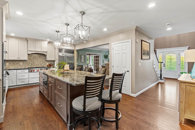 104 Windsor Dr, Auburn, NH 03032 - kitchen featuring built in appliances, a kitchen bar, a chandelier, tasteful backsplash, and a center island with sink
