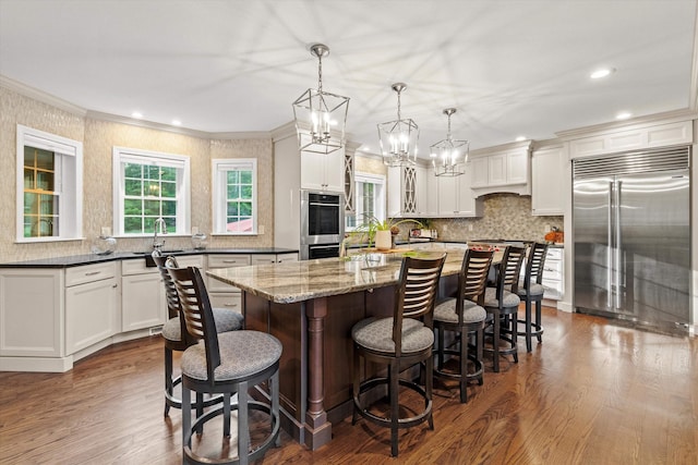 104 Windsor Dr, Auburn, NH 03032 - kitchen featuring appliances with stainless steel finishes, dark wood-style floors, decorative backsplash, a breakfast bar area, and ornamental molding